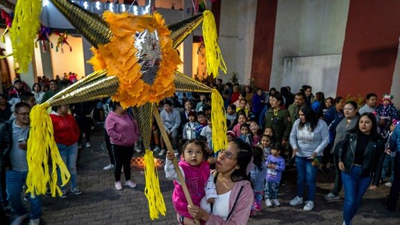 Ein Kind versucht auf dem Arm seiner Mutter auf einem Platz im Stadtzentrum eine Piñata zu spielen.