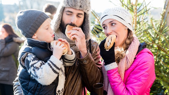 Familie isst Brötchen und Würste auf einem Weihnachtmarkt