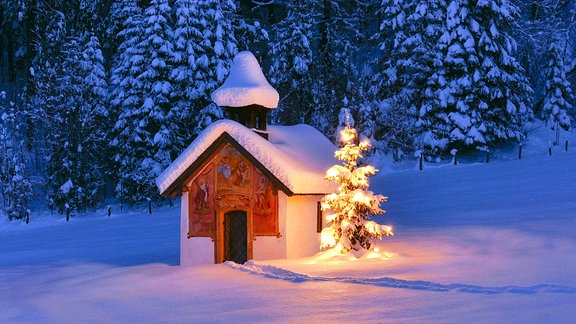 Ein beleuchteter Christbaum vor einer Kapelle im Winter
