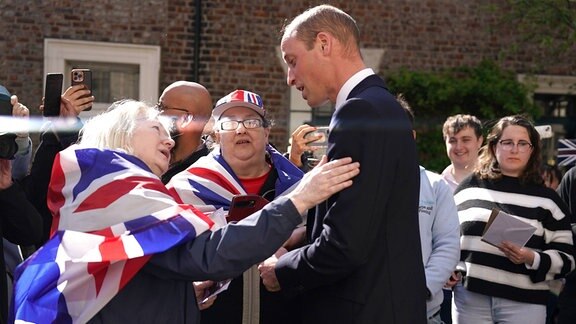 Prinz William spricht mit einer Frau, die in eine britische Fahne gehüllt ist.