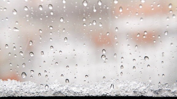 Schneeregen und Hagel zeigt sich in Tropfen und Schneematsch an einer Fensterscheibe