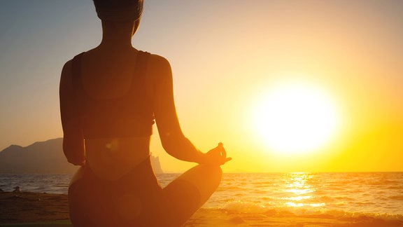Mädchen macht Yoga und meditiert am Strand