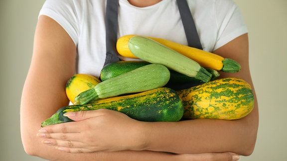 Eine Frau hat die Arme voll Zucchini.